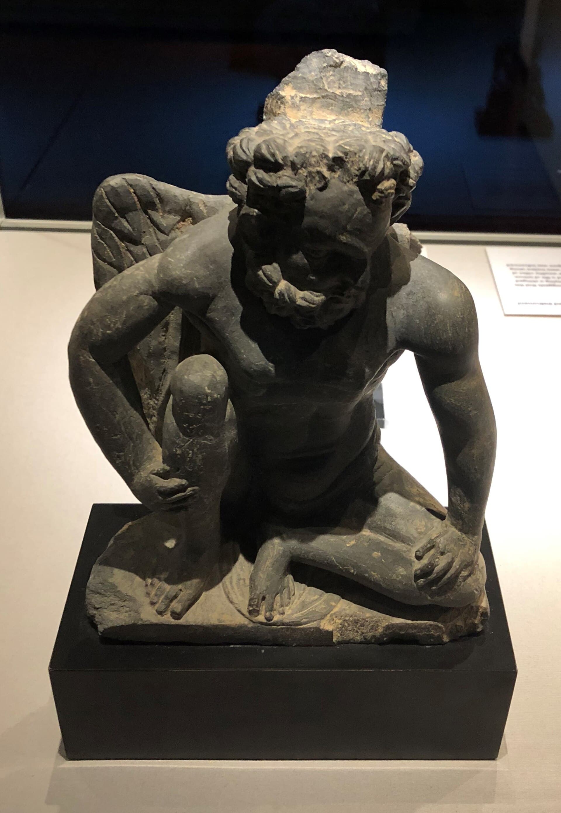 A third-century Gandharan relief carved in schist, showing Atlas as a straining support figure — the Greek god absorbed into Buddhist architecture in what is now Pakistan.